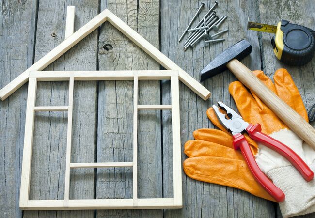 Kleines Holzhaus aus Stäben gebaut, Werkzeug daneben, Handschuhe, Hammer und Nägel